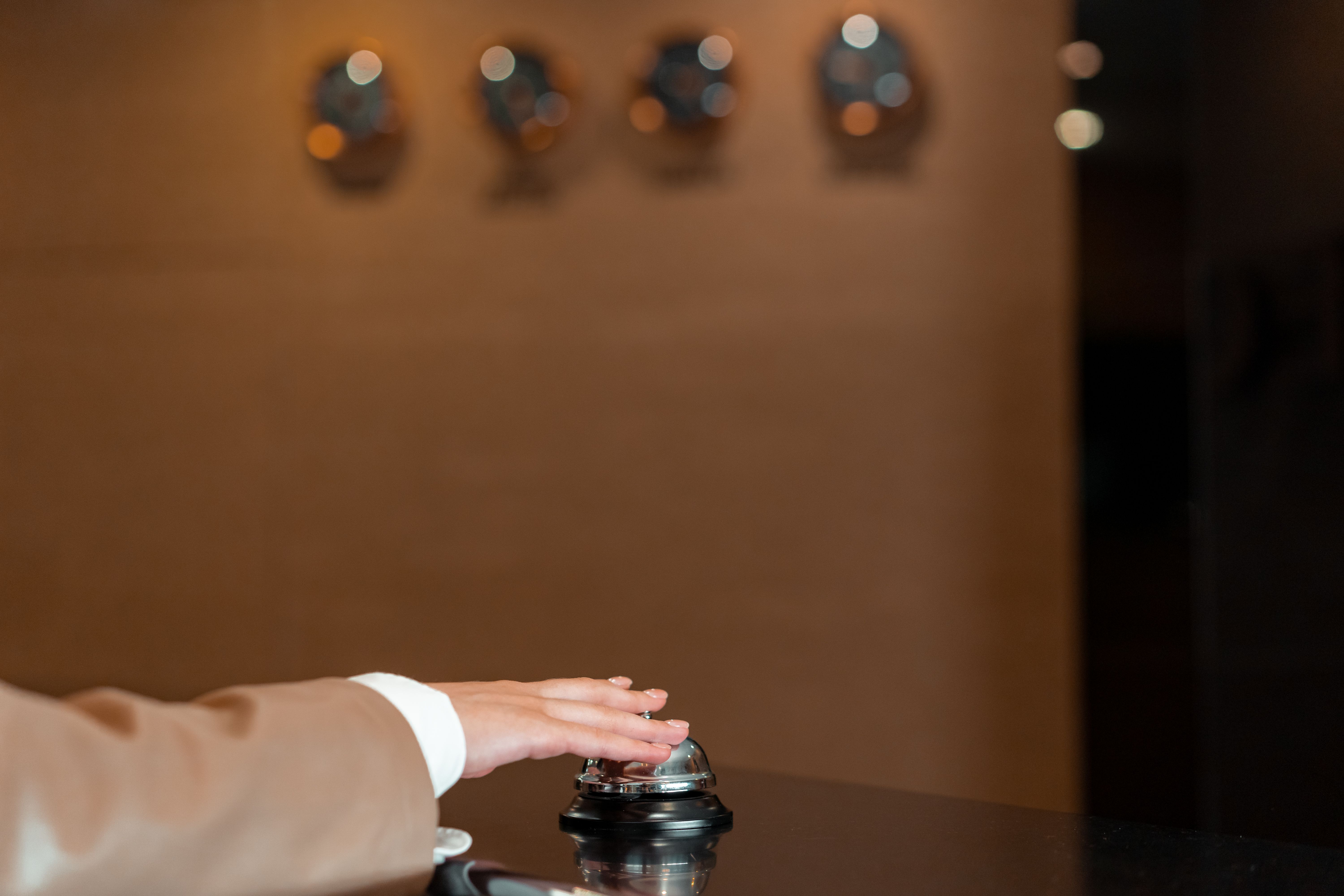 A hand pressing a hotel reception bell, symbolizing discreet, attentive hospitality.
