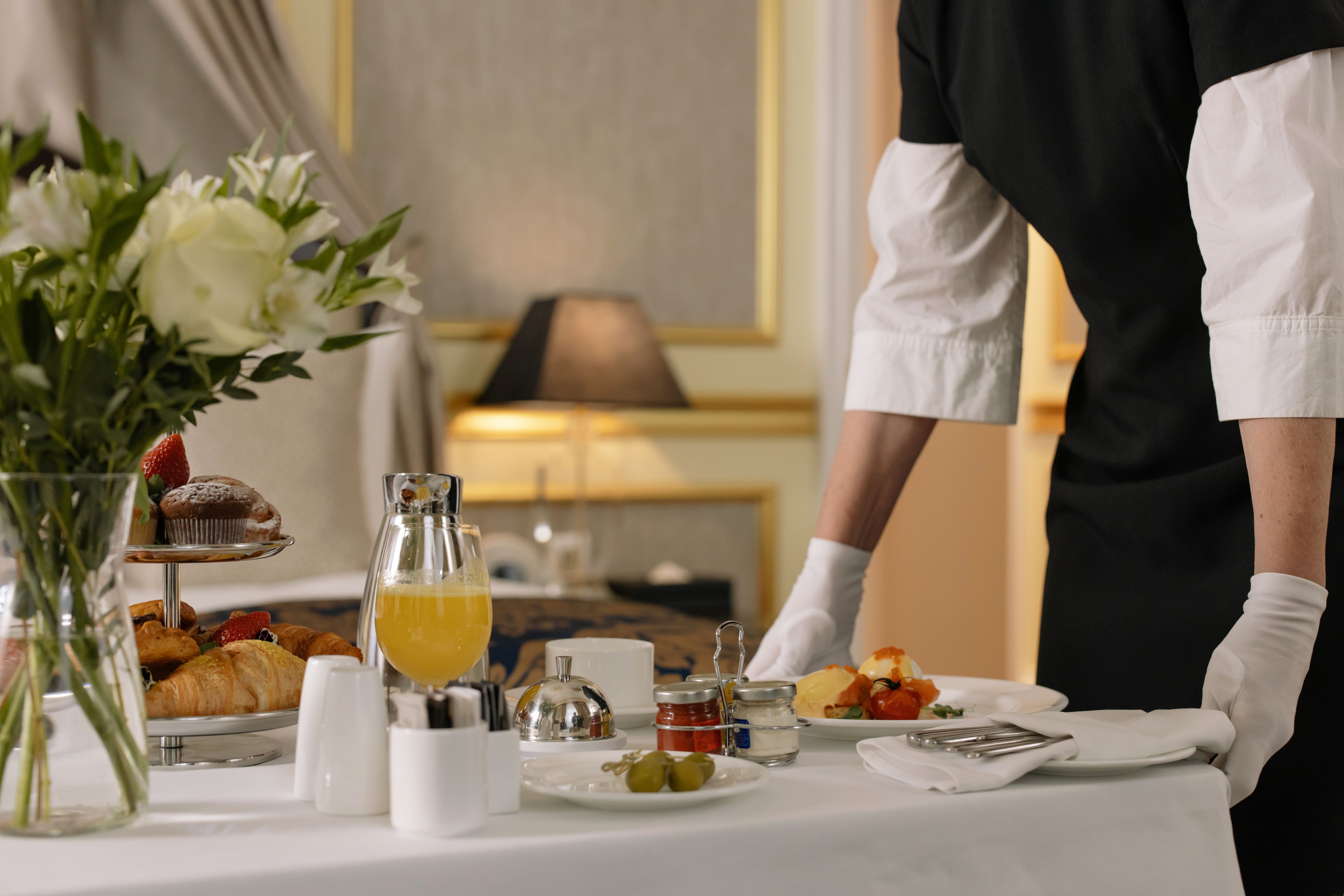A luxurious hotel room with an elegant breakfast setup, flowers, and assorted pastries.