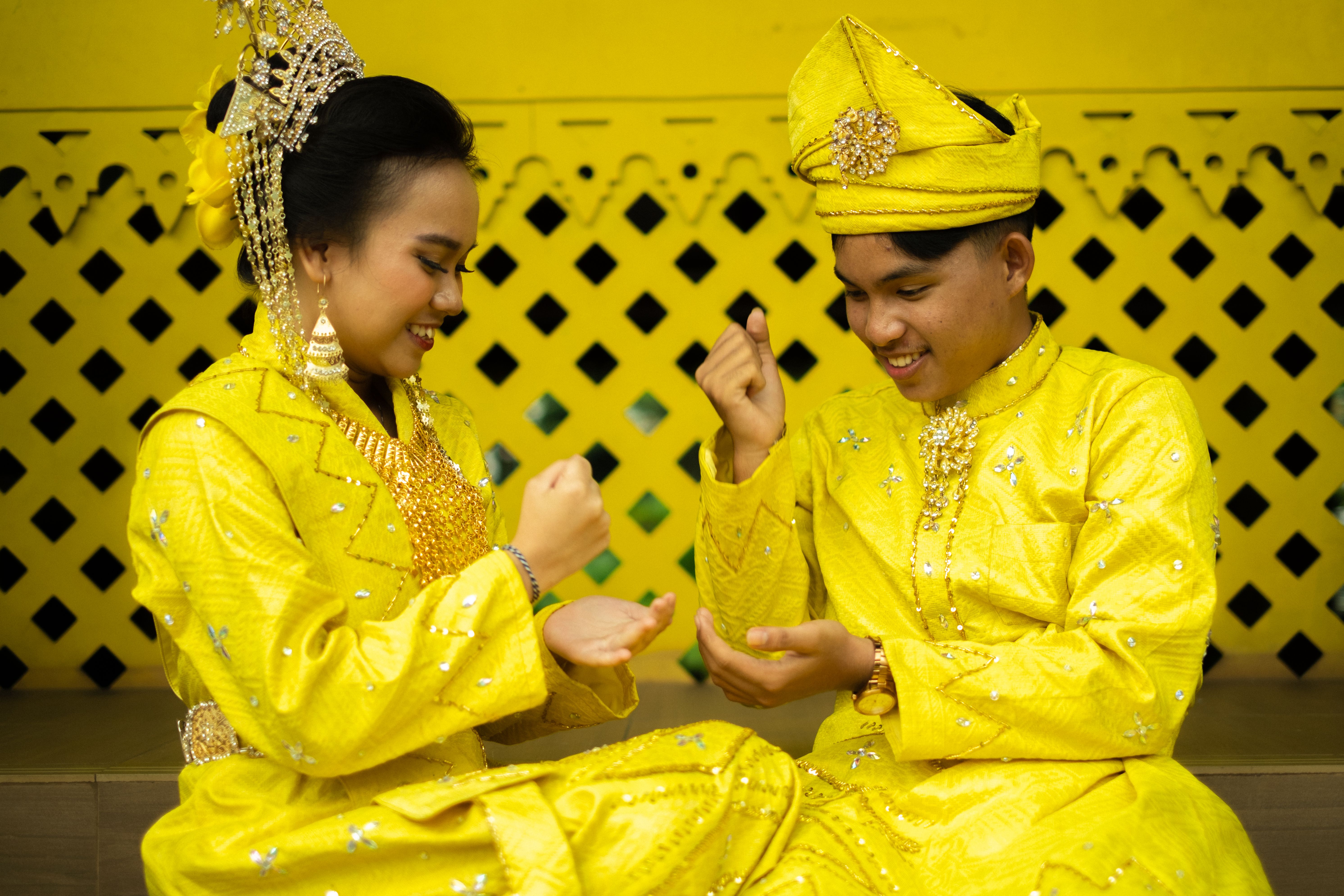 Two people in Malay traditional attire playing a cultural hand game