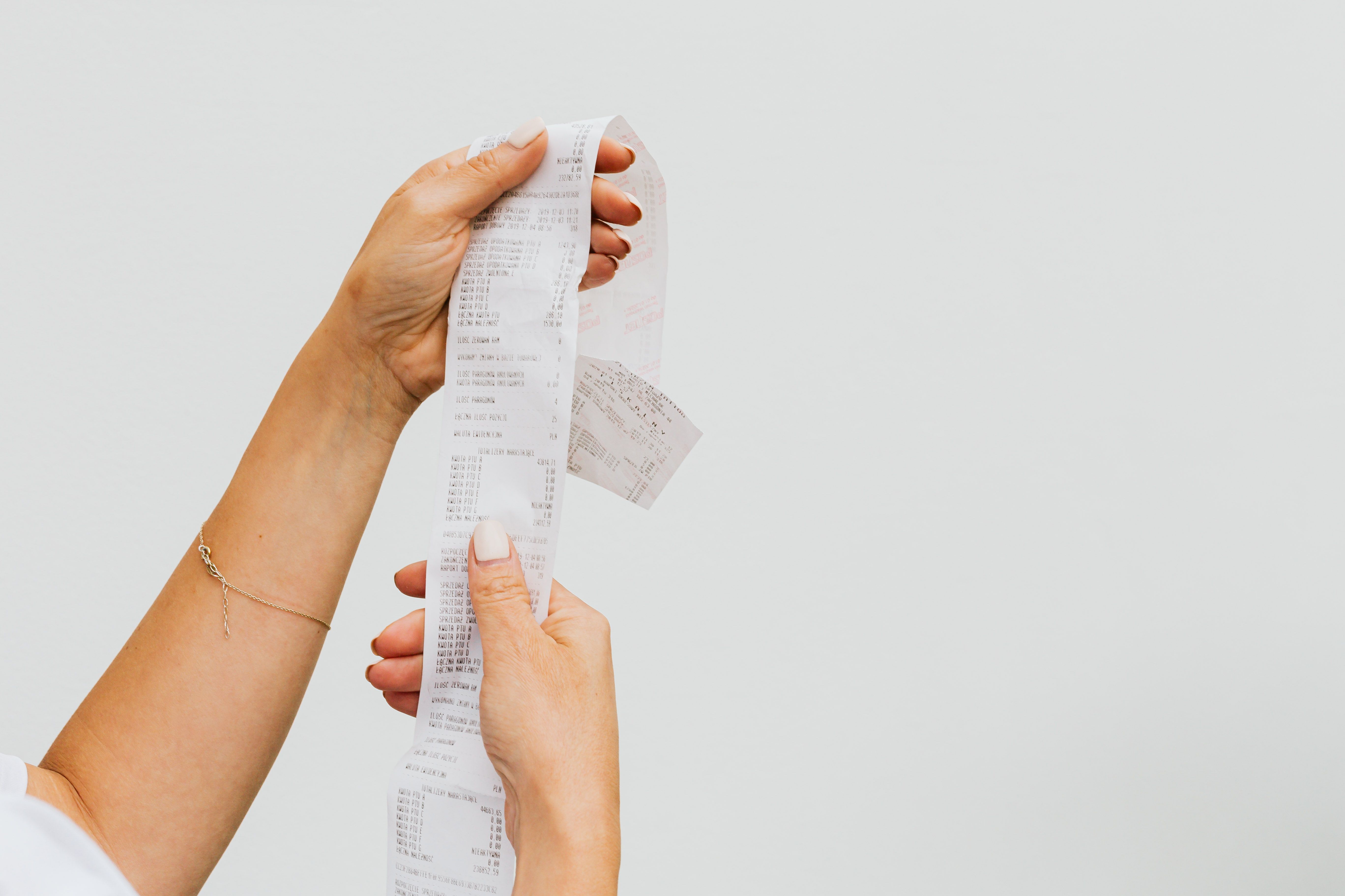 Person holding a long shopping receipt against a plain background, representing consumer purchase evidence